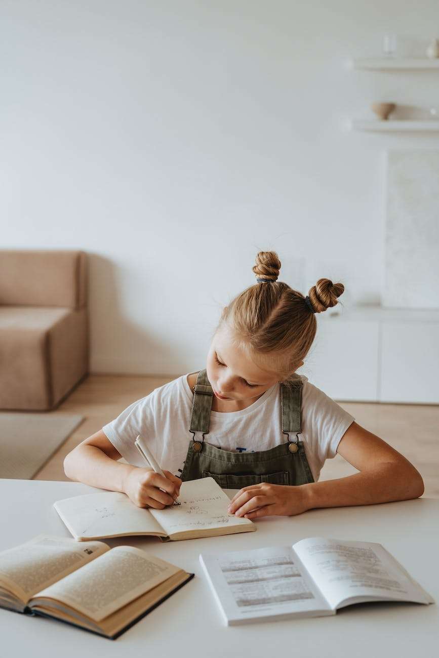 little girl writing on a notebook: how to teach writing in homeschool