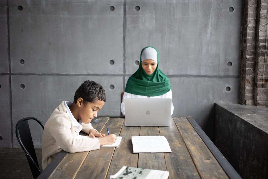 positive arabian mother using modern laptop while sitting together with son