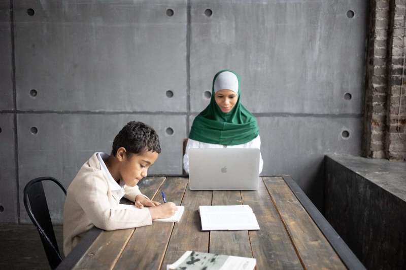 positive arabian mother using modern laptop while sitting together with son