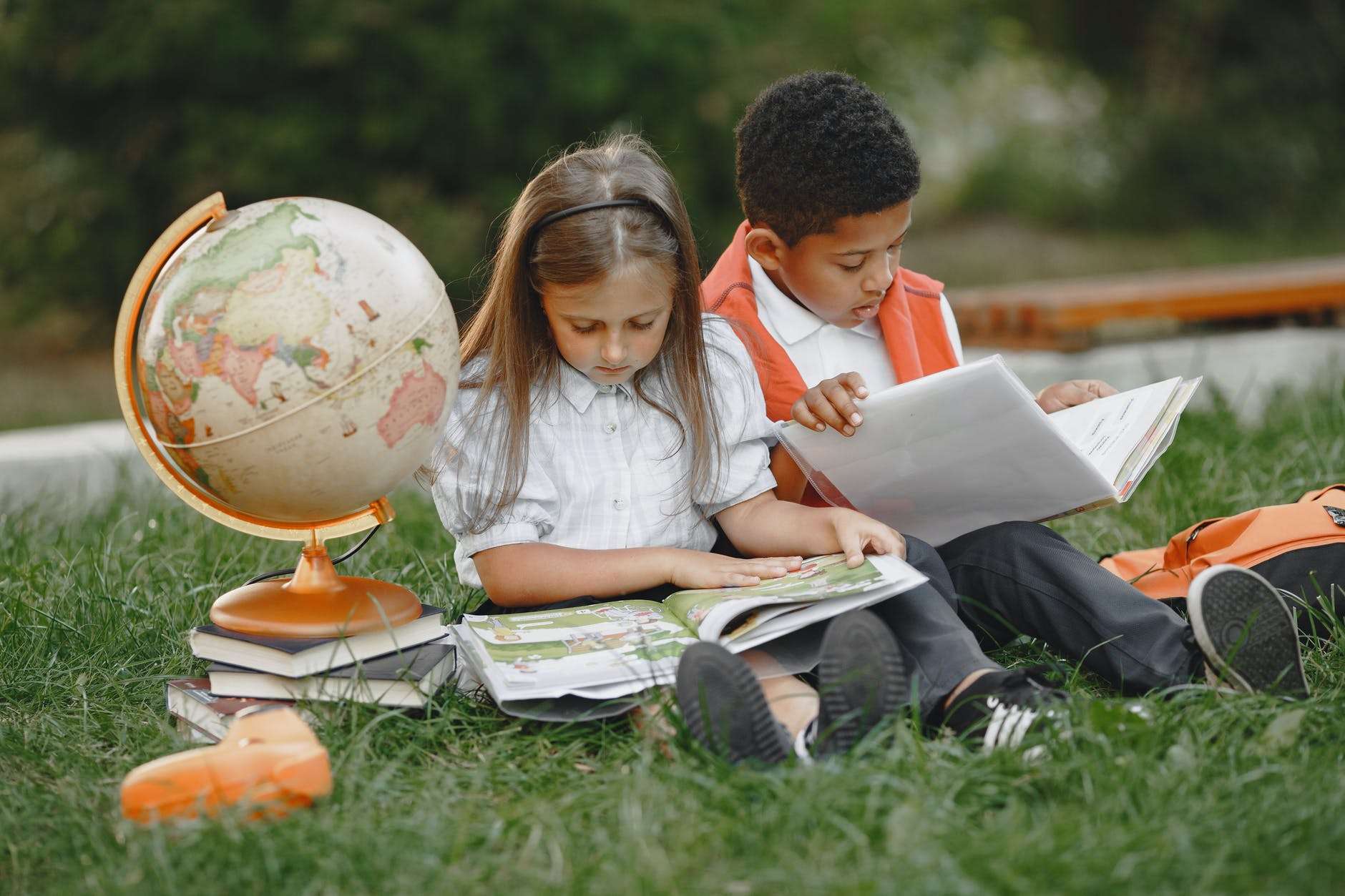 a boy and a girl sitting on grass with textbooks and a globe: should I homeschool my child?