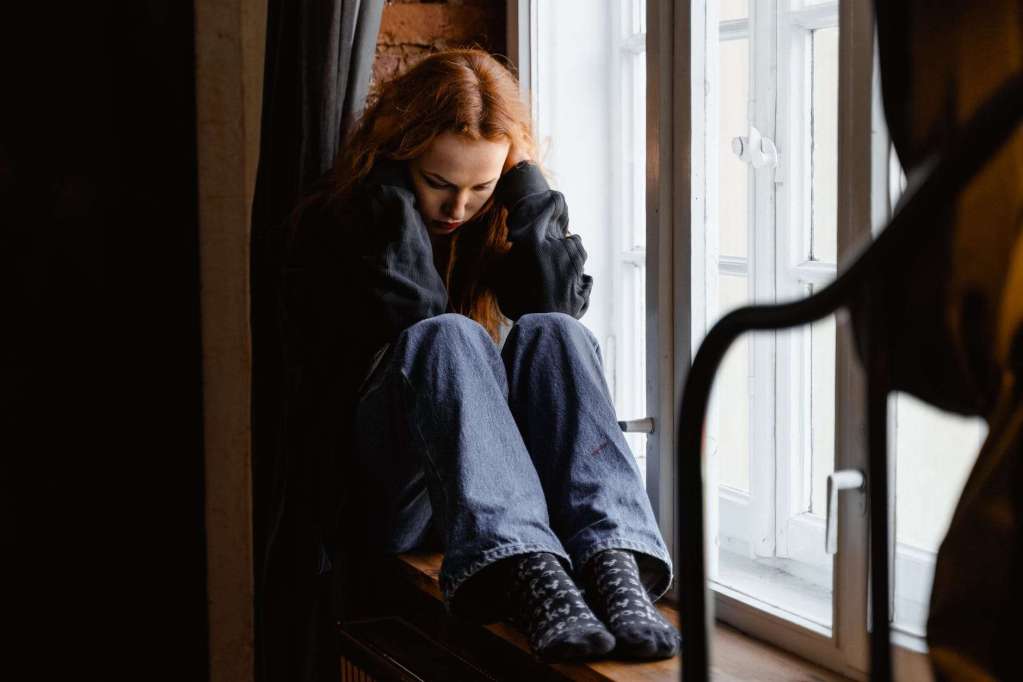 depressed woman sitting by the window: choose a growth mindset for homeschoolers