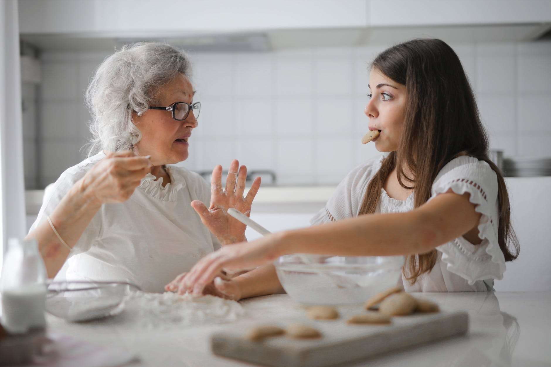 pensive grandmother with granddaughter having interesting conversation while cooking together in light modern kitchen and discussing why homeschool is hard