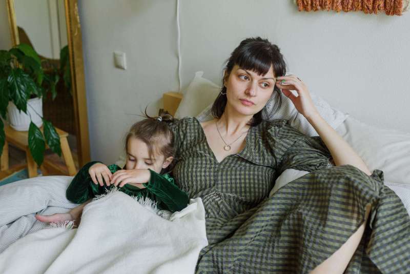 tired mother with cute daughter resting on bed in cozy room