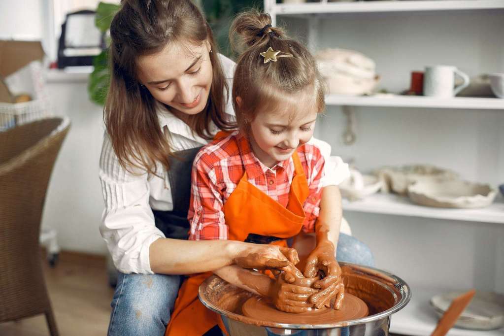 female potter teaching daughter molding on pottery wheel: deschooling acknowledges that we honour all the different kinds of learning