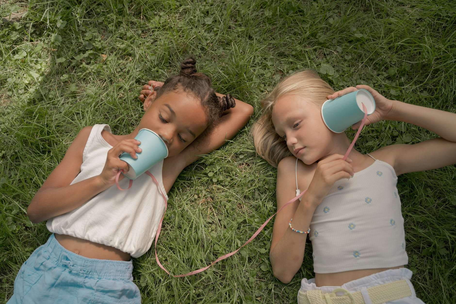 two teenage girls laying on grass and playing telephone call using paper cups on string: homeschool mom personal vision