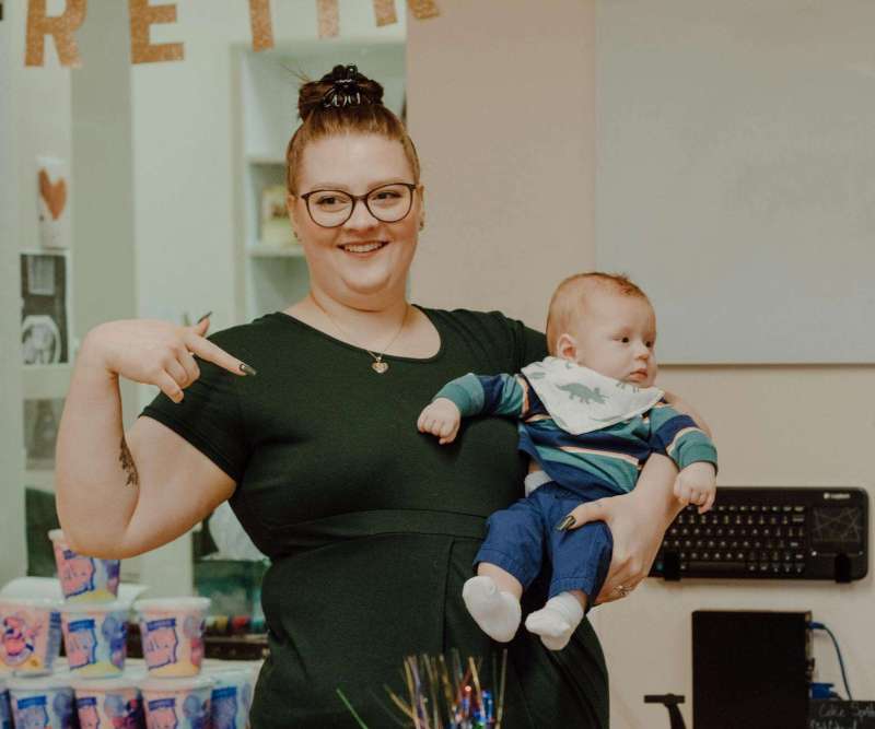 smiling woman in glasses pointing at baby on arms