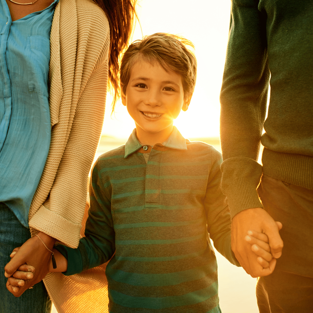 Child holding parents' hands in golden sunset light — life coaching for homeschool moms strengthens your whole family