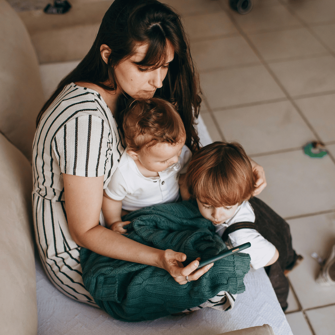 Overwhelmed homeschool mom sitting on the floor with two young children — life coaching for homeschool moms helps you carry less and enjoy more